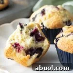 Three blueberry muffins on a white plate, one cut in half.