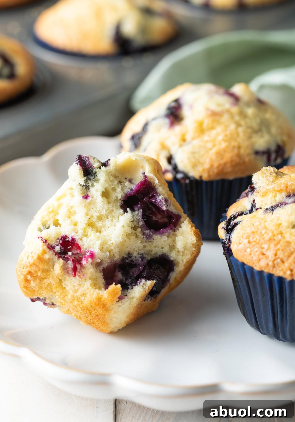 Three blueberry muffins on a white plate, one cut in half. 