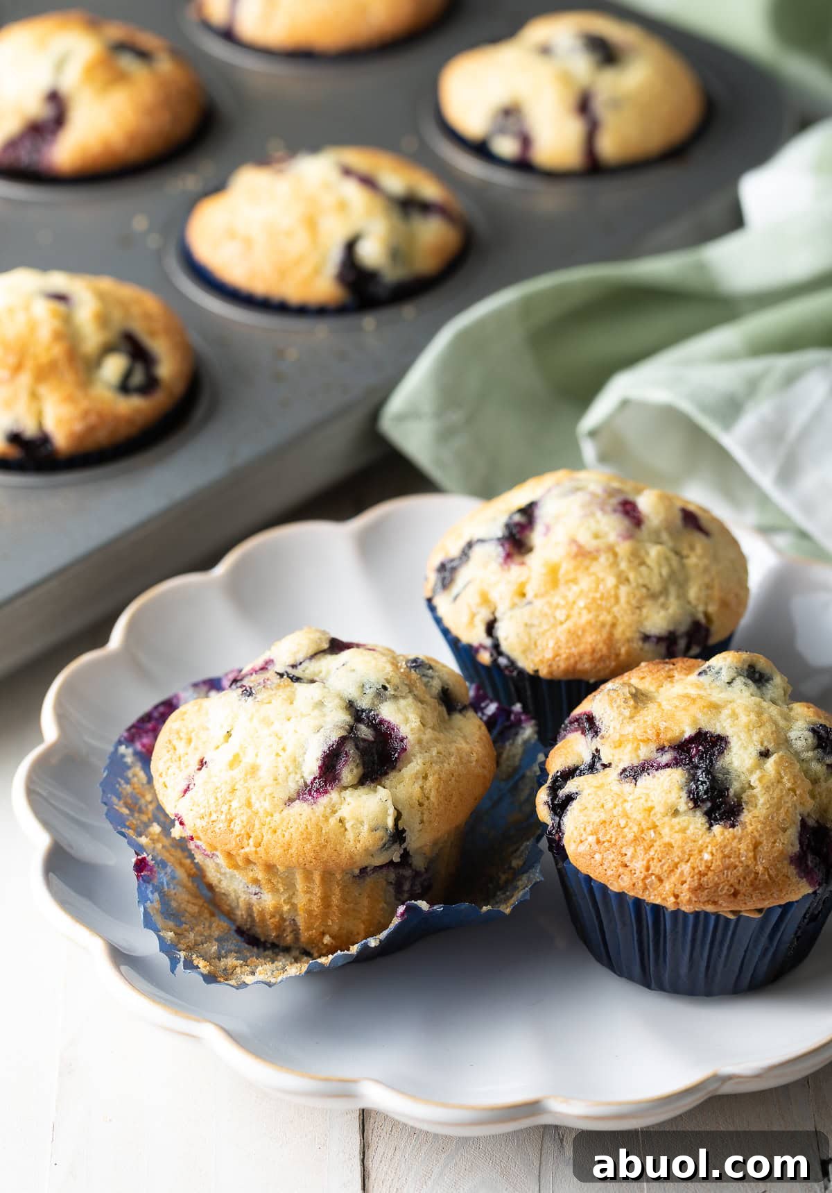 A plate of three blueberry muffins made from a homemade blueberry muffins recipe.