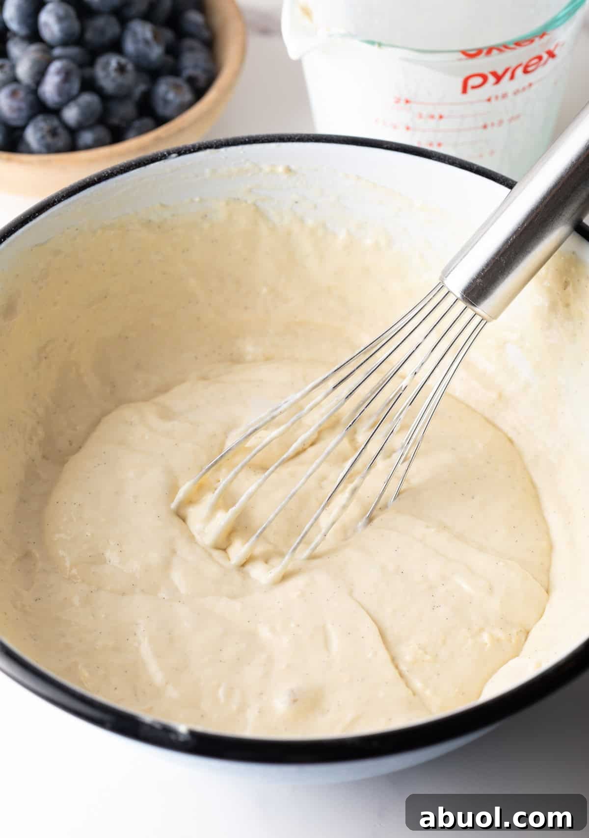 White bowl of pancake batter being stirred with a whisk.