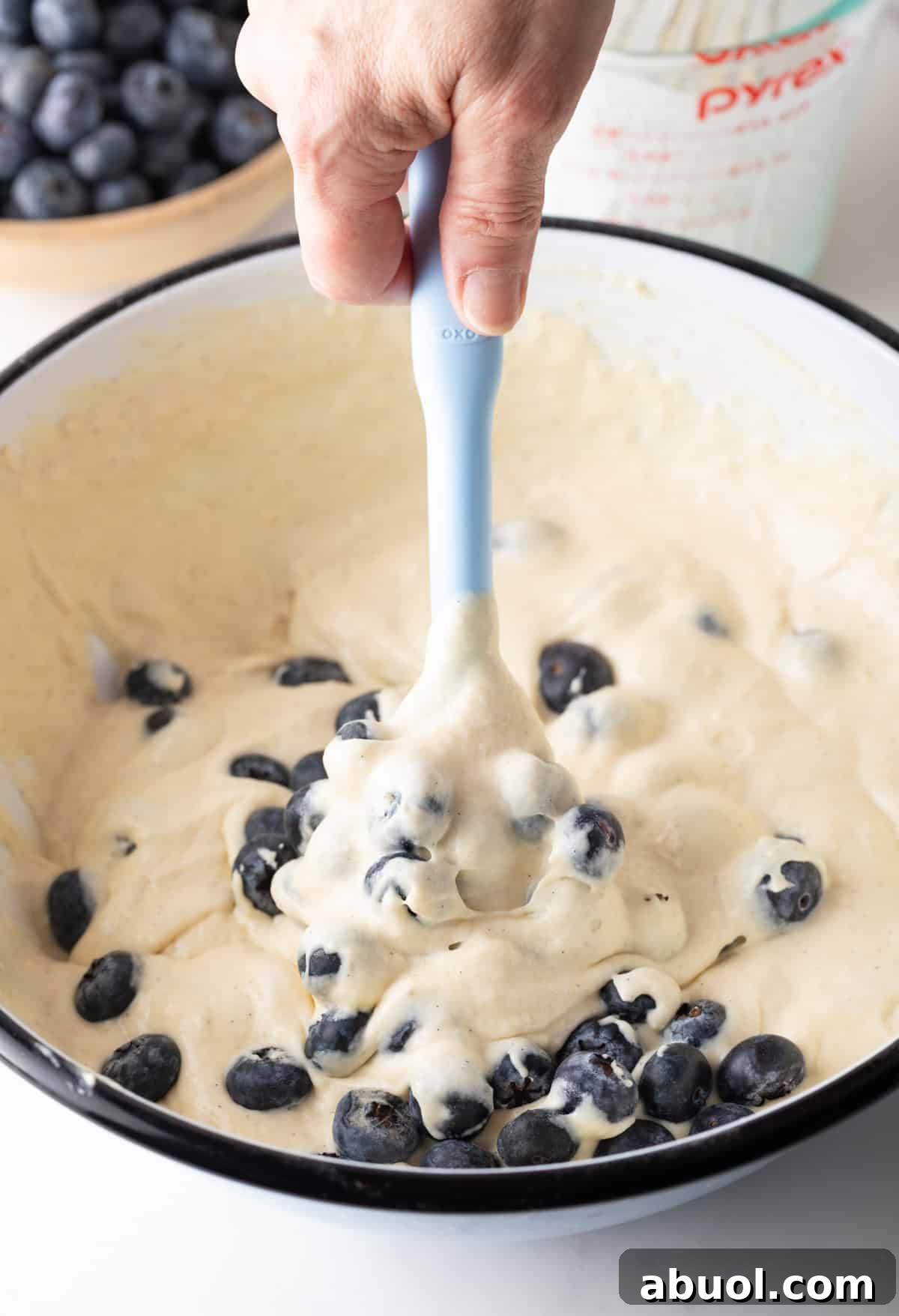 Using a light blue spatula to fold blueberries into the pancake batter.