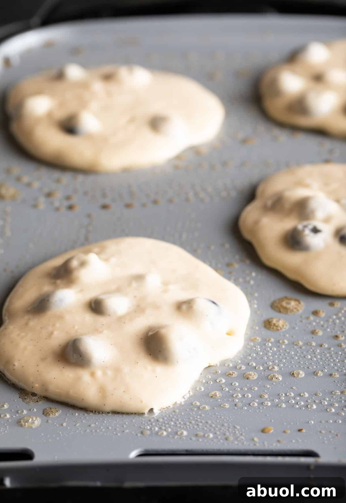 4 raw blueberry pancakes cooking on a griddle.