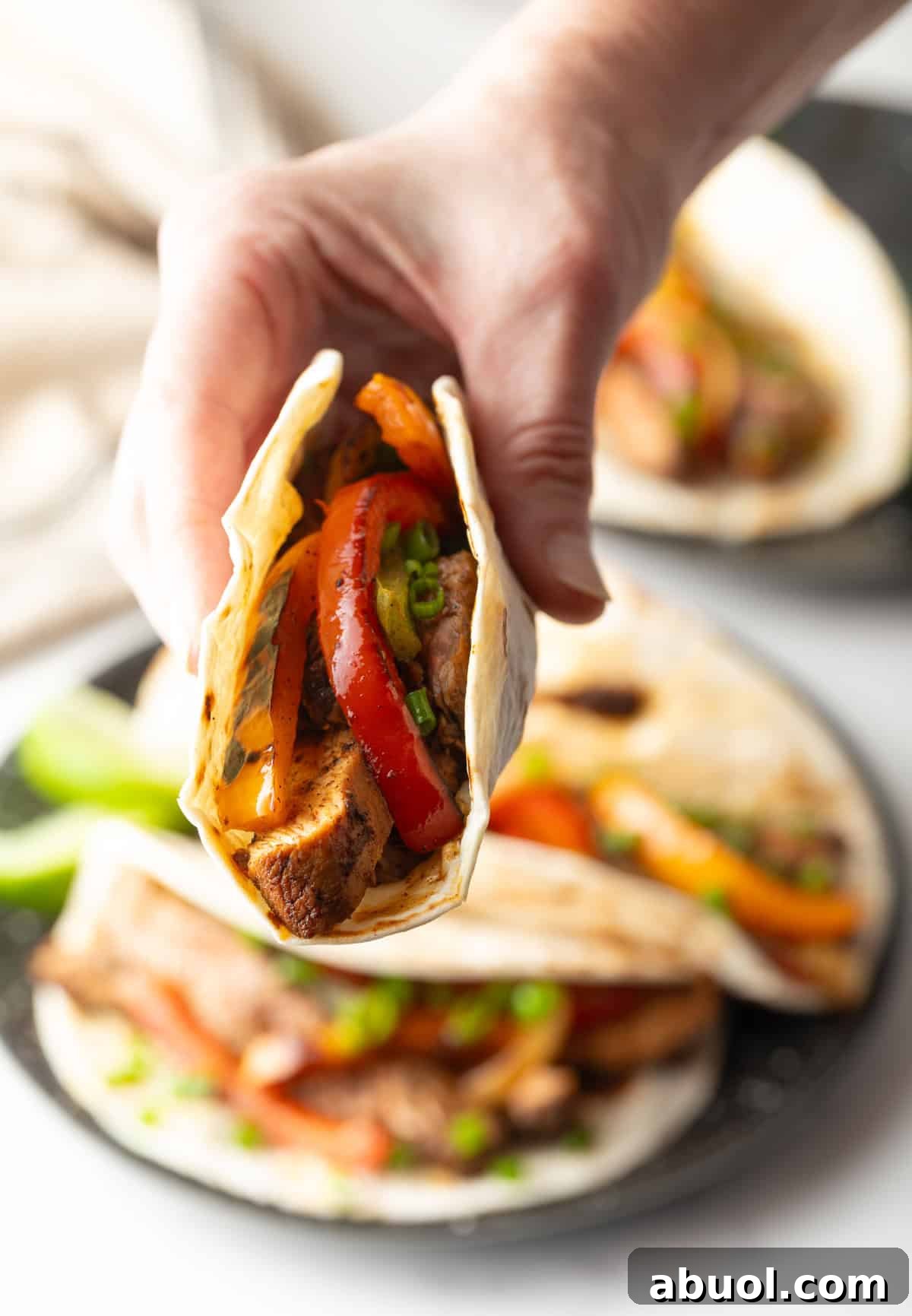 A hand holding a tortilla filled with a homemade steak fajita recipe.