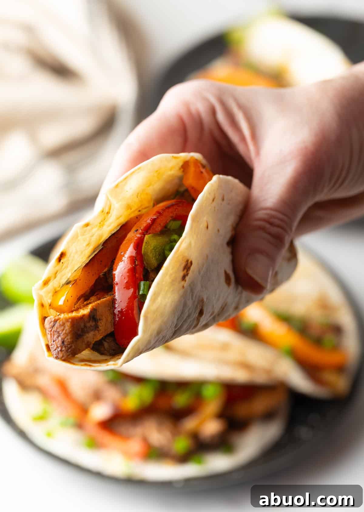 A hand holding a tortilla filled with a homemade chicken fajita mixture.