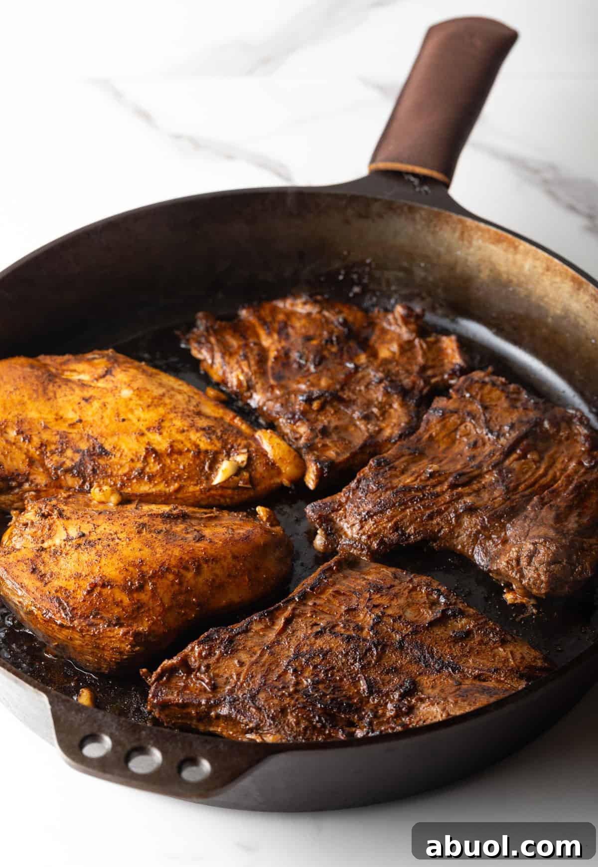 Five steaks are being seared in a black skillet.