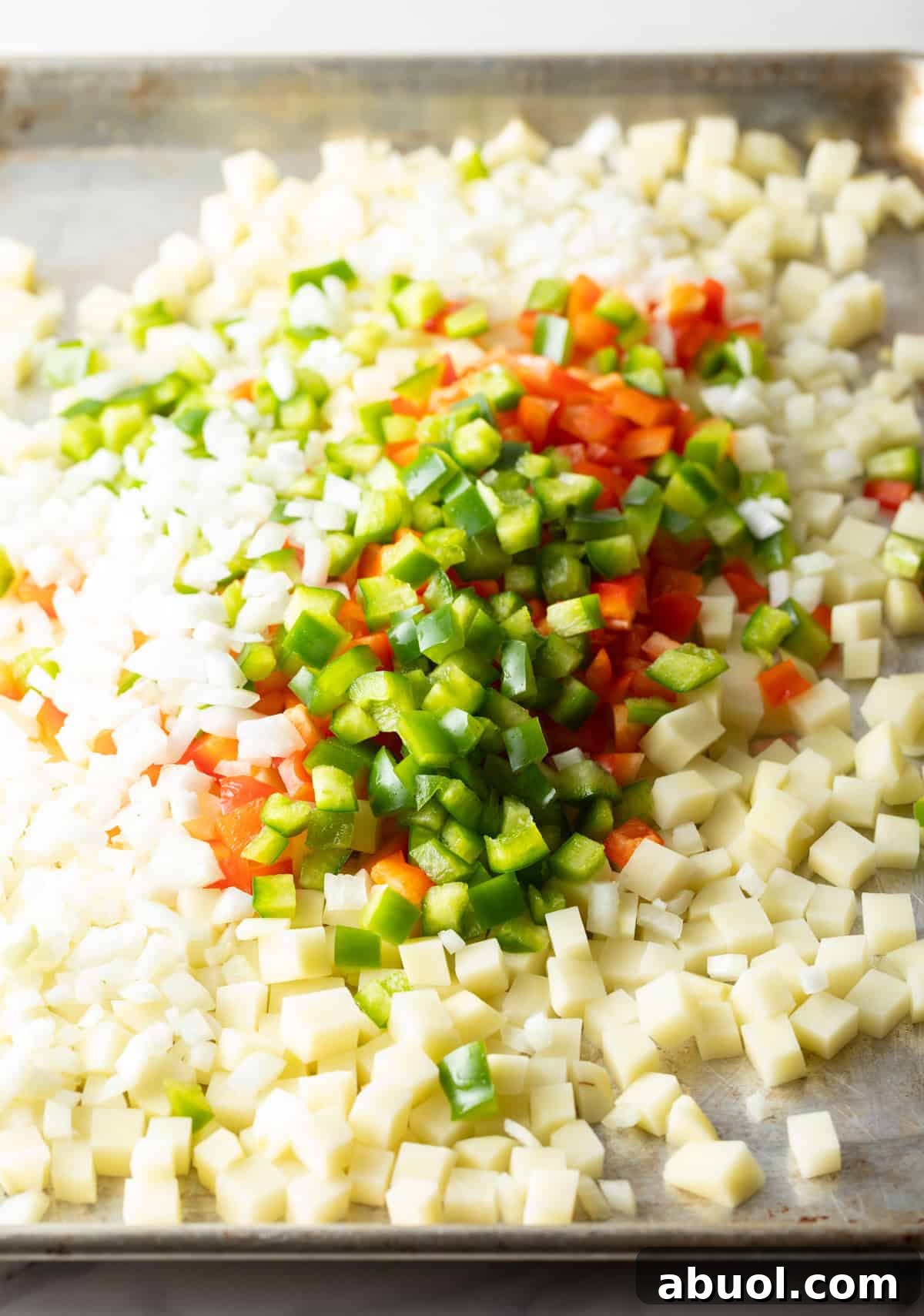 A baking sheet topped with diced potatoes, onions, and bell peppers.