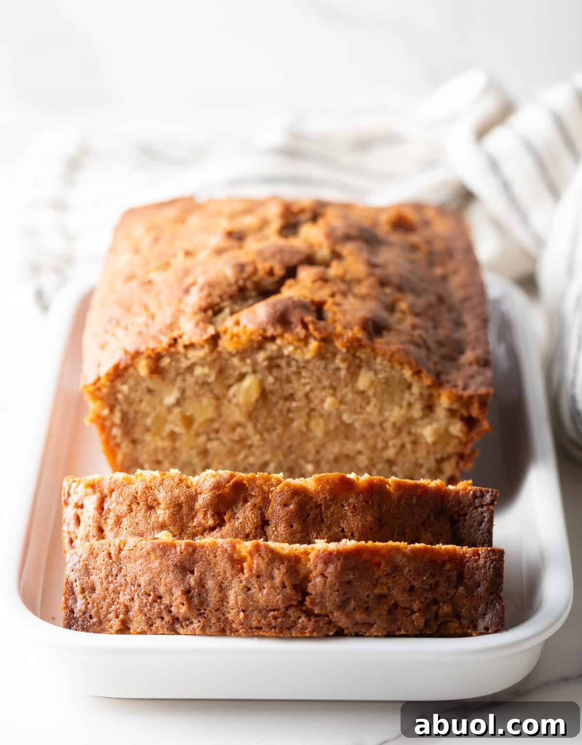 A freshly baked apple bread recipe sitting in a white baking dish, with a slice laying against the edge of the dish.