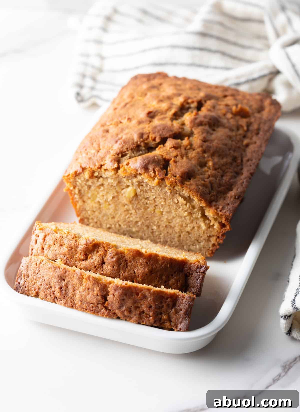 An apple bread recipe on a white dish with two slices cut in front of the loaf.