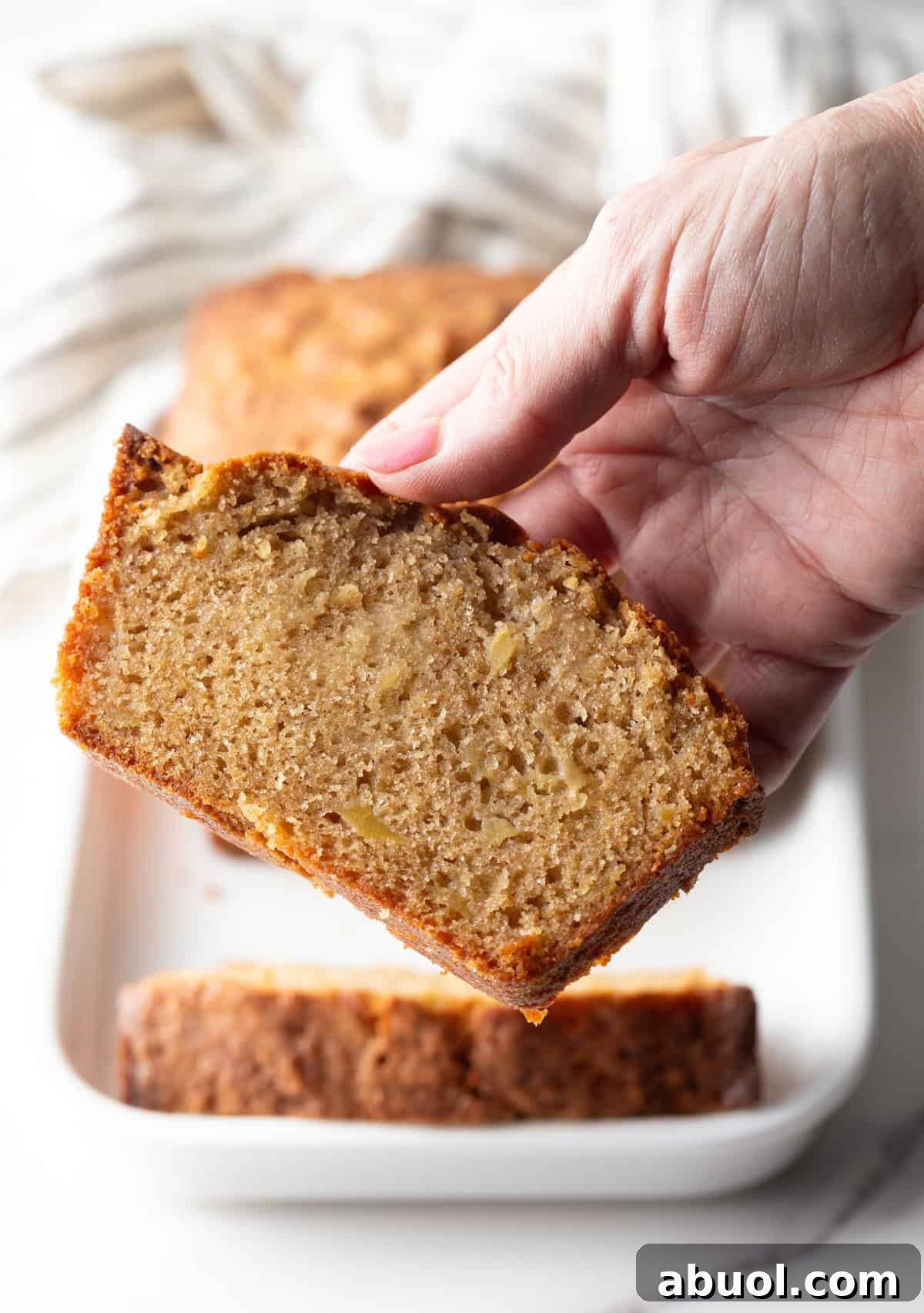 A hand is holding a slice of cinnamon apple bread.