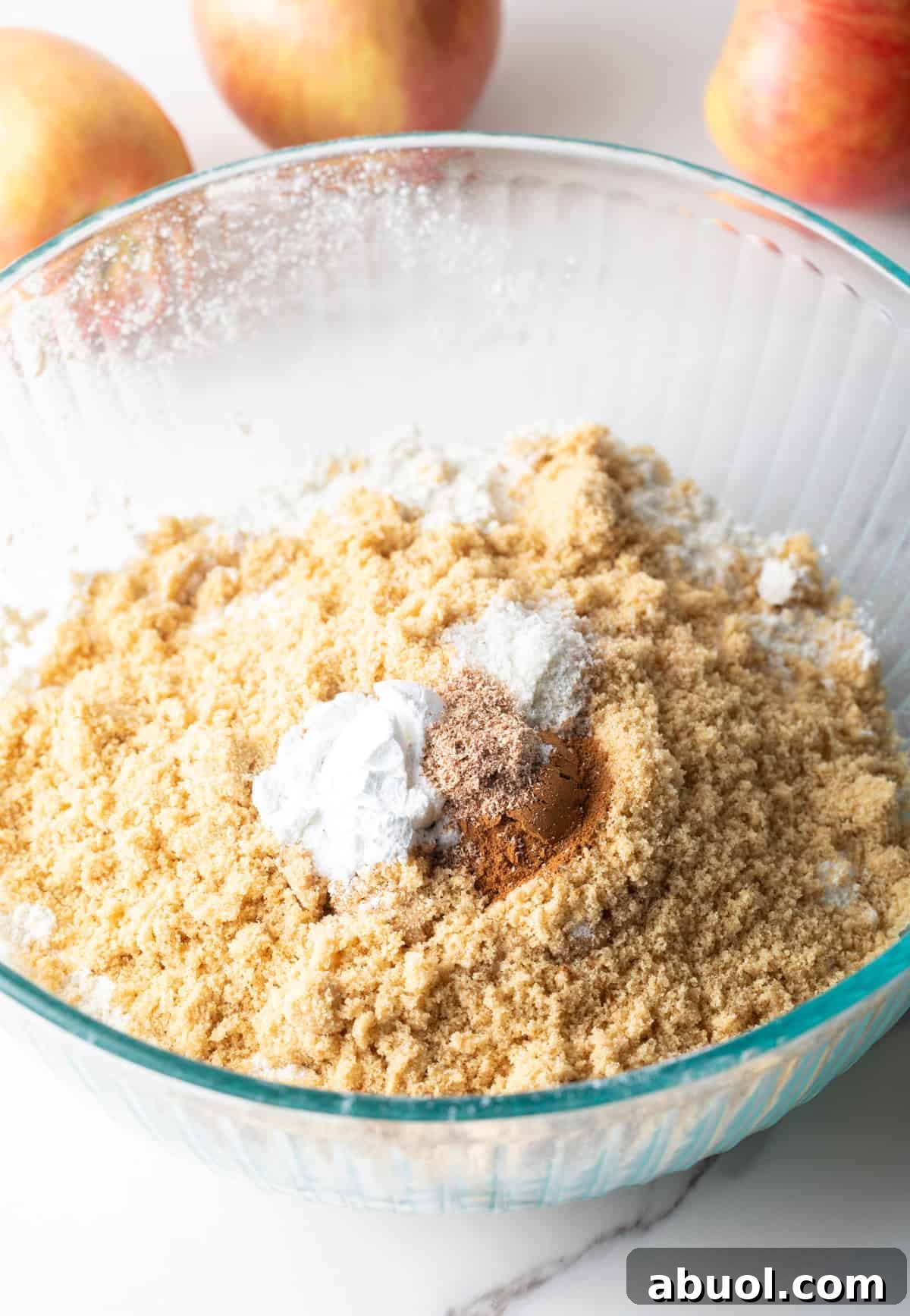 A flour and spice mixture is sitting in a glass bowl for an apple bread recipe.