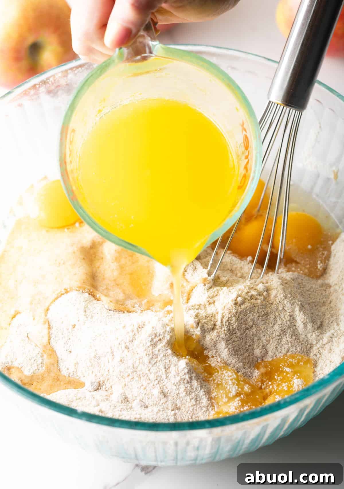 Melted butter is being poured over a spiced apple bread mixture in a glass bowl.